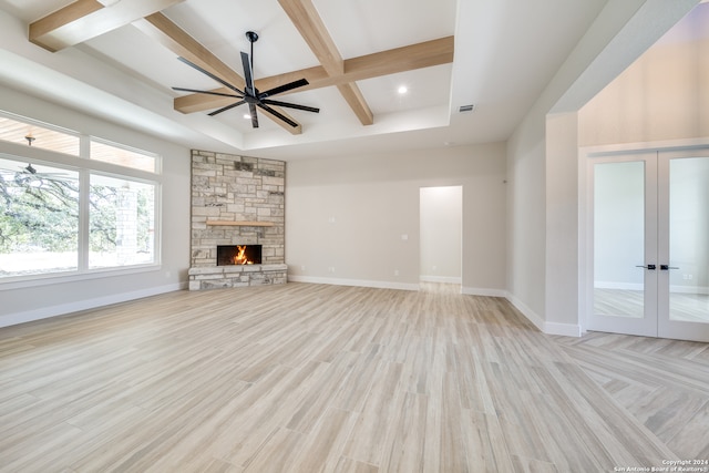 unfurnished living room featuring french doors, light hardwood / wood-style floors, a stone fireplace, and beam ceiling