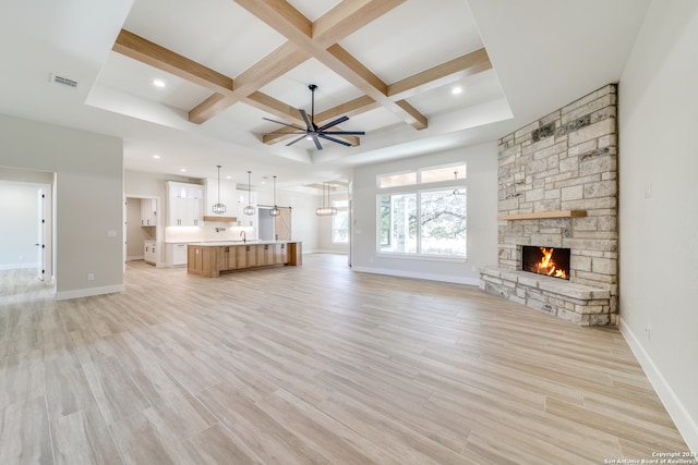 unfurnished living room with a fireplace, light hardwood / wood-style floors, coffered ceiling, ceiling fan, and beam ceiling