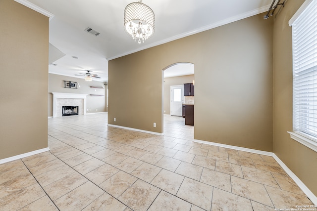 interior space featuring ornamental molding, a wealth of natural light, a tile fireplace, and ceiling fan with notable chandelier