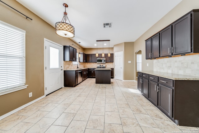 kitchen featuring decorative backsplash, appliances with stainless steel finishes, decorative light fixtures, and a kitchen island