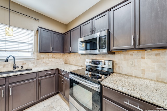 kitchen with decorative backsplash, light stone counters, appliances with stainless steel finishes, dark brown cabinetry, and sink