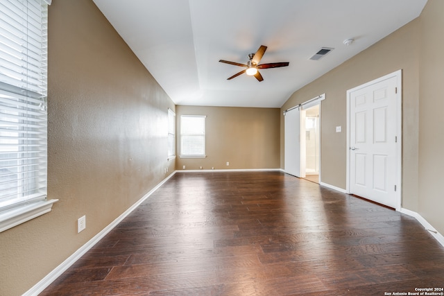 empty room with lofted ceiling, a barn door, dark hardwood / wood-style floors, and ceiling fan