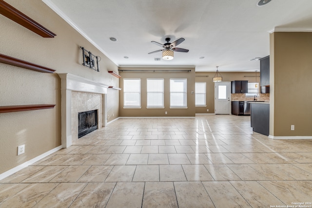 unfurnished living room with ornamental molding, sink, a tile fireplace, and ceiling fan