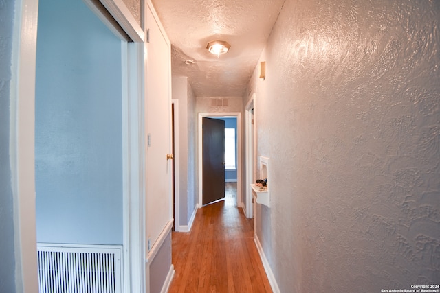 corridor with wood-type flooring and a textured ceiling