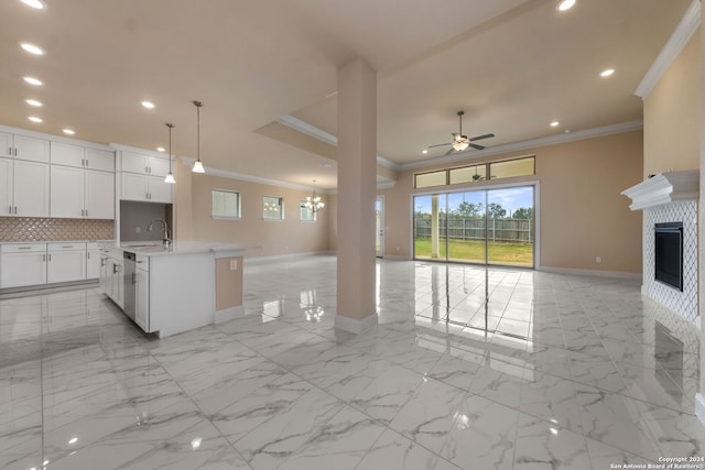 kitchen featuring hanging light fixtures, backsplash, a center island with sink, ornamental molding, and white cabinetry