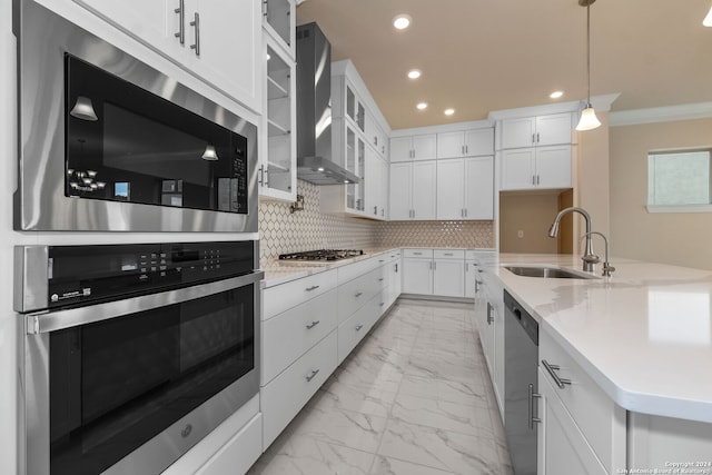 kitchen featuring wall chimney range hood, white cabinetry, sink, pendant lighting, and stainless steel appliances