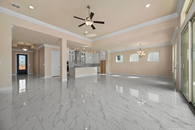 unfurnished living room with ornamental molding, a healthy amount of sunlight, ceiling fan with notable chandelier, and a raised ceiling