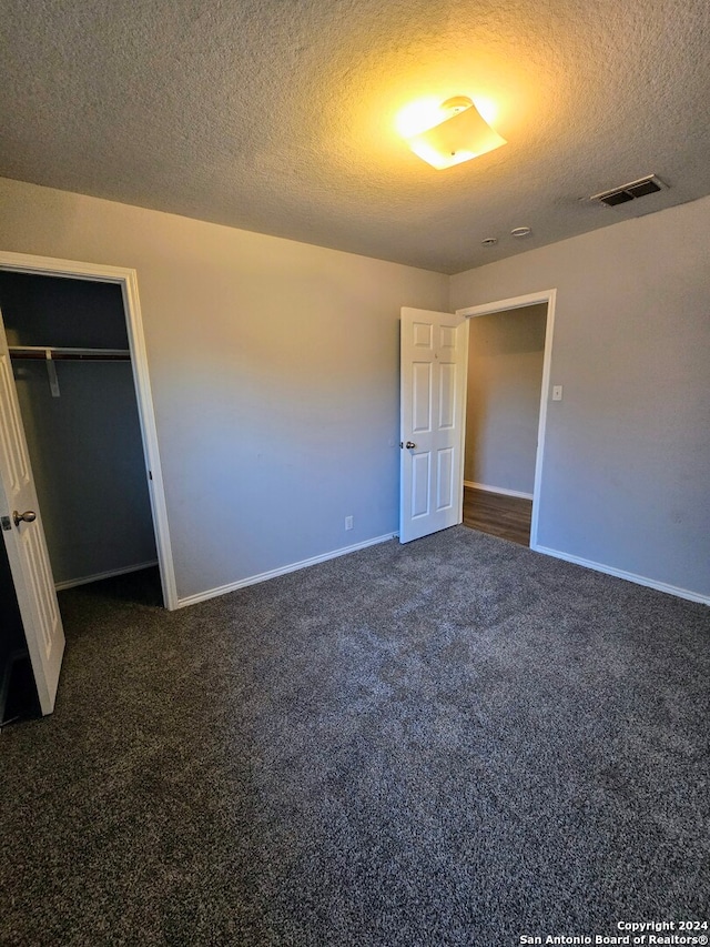 unfurnished bedroom with a closet, a textured ceiling, and dark colored carpet