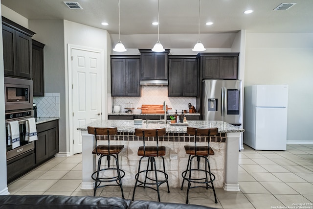 kitchen featuring light stone counters, a kitchen island with sink, decorative light fixtures, and stainless steel appliances