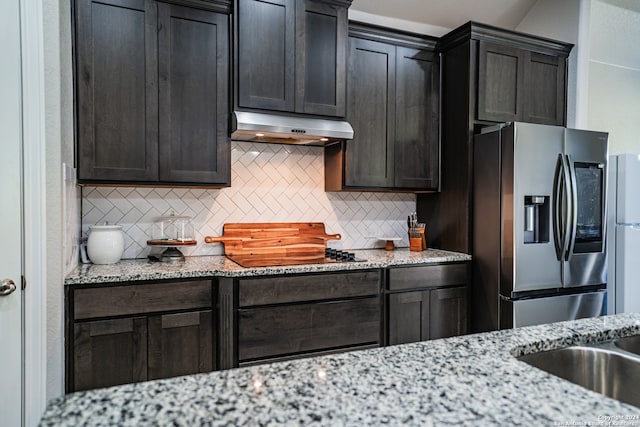 kitchen with decorative backsplash, dark brown cabinets, stainless steel fridge with ice dispenser, light stone counters, and black cooktop