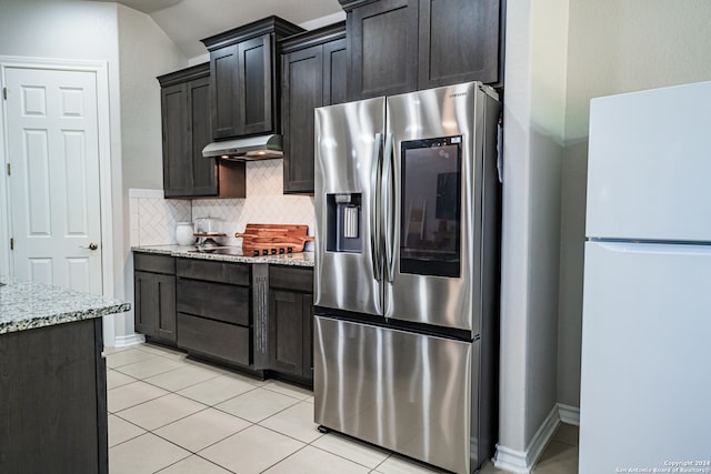 kitchen featuring decorative backsplash, stainless steel fridge, light stone counters, and white refrigerator