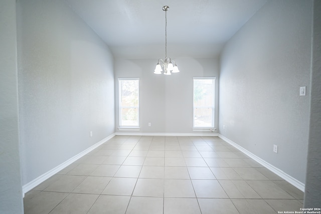 tiled empty room featuring a chandelier and vaulted ceiling