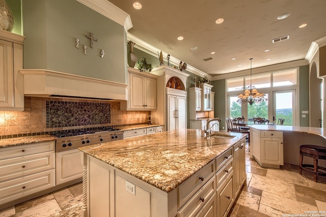 kitchen with sink, decorative light fixtures, ornamental molding, a chandelier, and a center island with sink