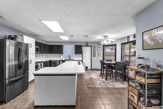 kitchen featuring dark tile patterned flooring, a center island, appliances with stainless steel finishes, a textured ceiling, and ceiling fan