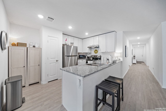 kitchen featuring light hardwood / wood-style flooring, kitchen peninsula, stainless steel appliances, light stone countertops, and white cabinetry