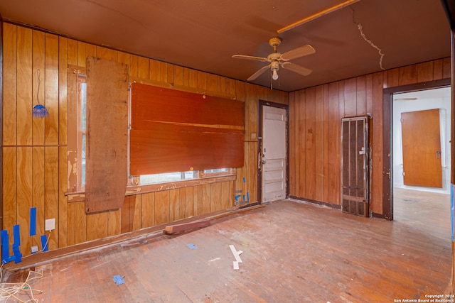 unfurnished room with ceiling fan, wood-type flooring, and wood walls