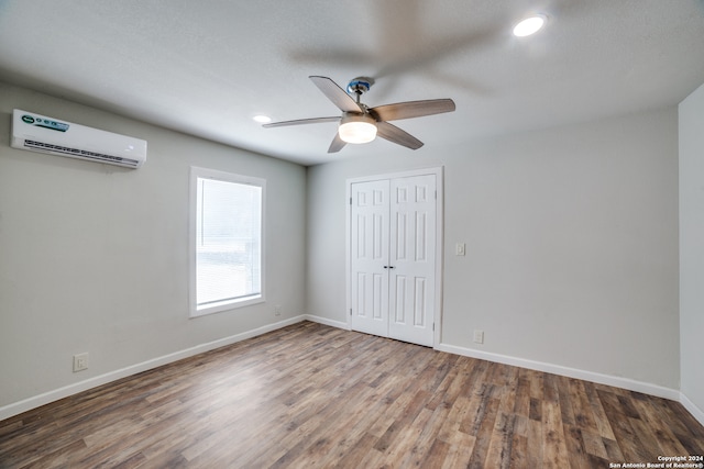 empty room with a wall unit AC, dark wood-type flooring, and ceiling fan