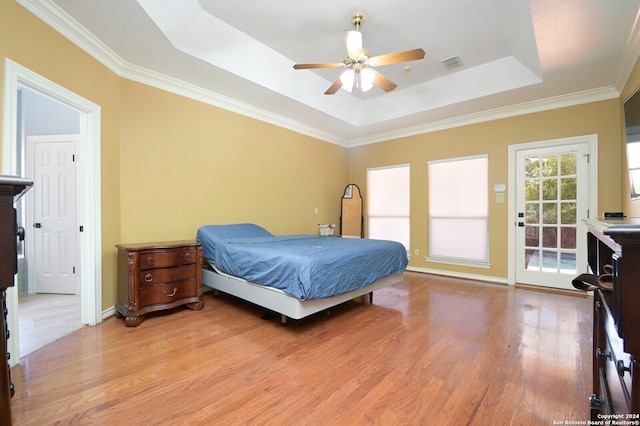 bedroom featuring access to exterior, light wood-type flooring, ornamental molding, a tray ceiling, and ceiling fan