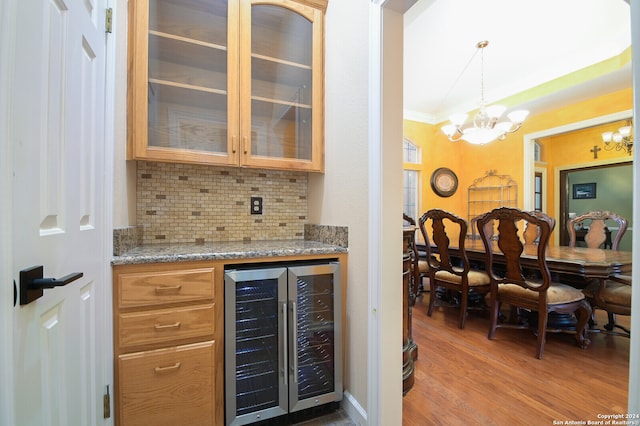 bar featuring beverage cooler, light stone counters, decorative light fixtures, hardwood / wood-style flooring, and ornamental molding