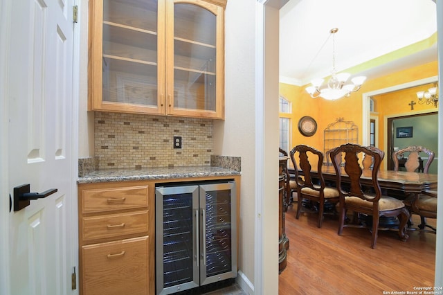 bar featuring wine cooler, a chandelier, decorative backsplash, light wood-type flooring, and decorative light fixtures