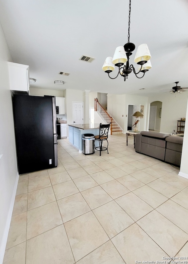 kitchen with decorative light fixtures, light tile patterned floors, white cabinets, ceiling fan with notable chandelier, and stainless steel refrigerator