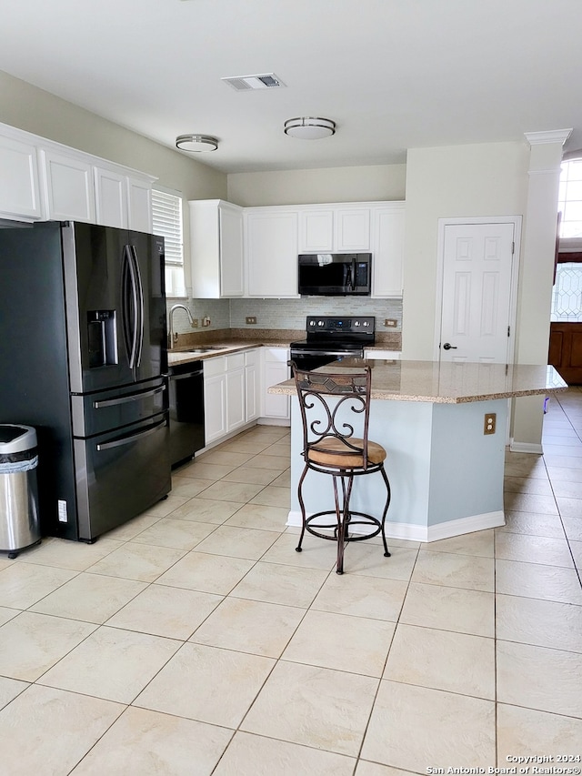 kitchen with black appliances, a center island, a kitchen breakfast bar, white cabinets, and light stone counters