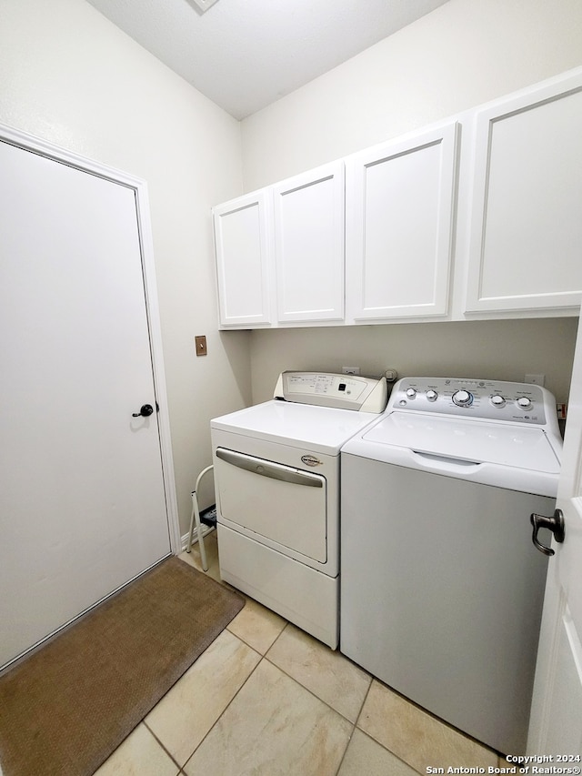 clothes washing area featuring cabinets, washing machine and clothes dryer, and light tile patterned floors