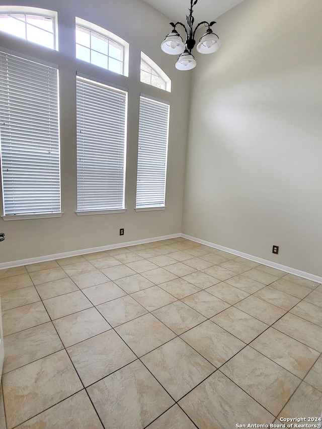 tiled empty room featuring an inviting chandelier