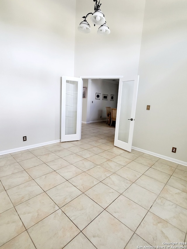 tiled empty room with a towering ceiling, a notable chandelier, and french doors