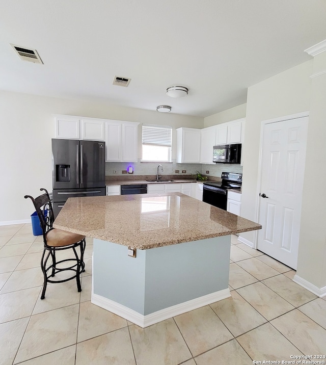 kitchen with a breakfast bar area, black appliances, a center island, white cabinetry, and light stone counters