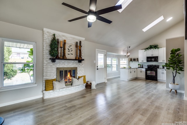 living room with light hardwood / wood-style flooring, a skylight, ceiling fan with notable chandelier, and a fireplace