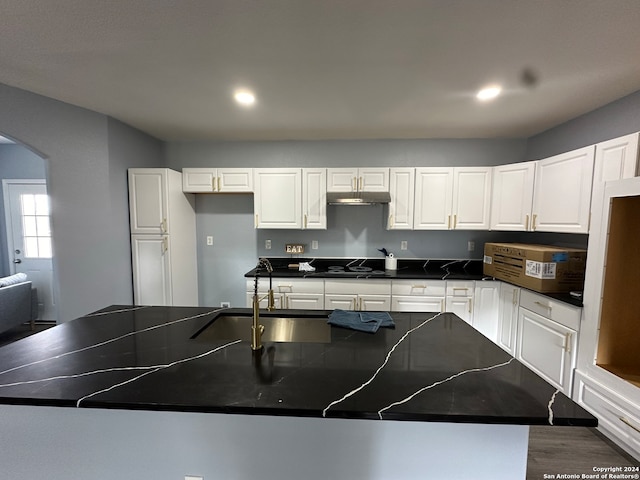 kitchen with white cabinets, an island with sink, cooktop, dark wood-type flooring, and sink