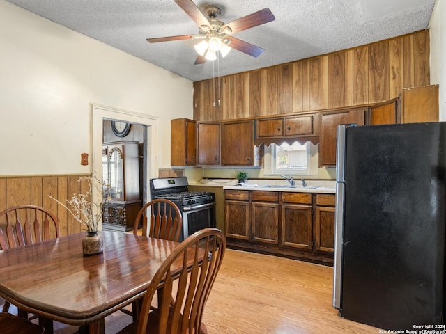 kitchen featuring stainless steel fridge, a textured ceiling, light hardwood / wood-style flooring, range with gas stovetop, and sink