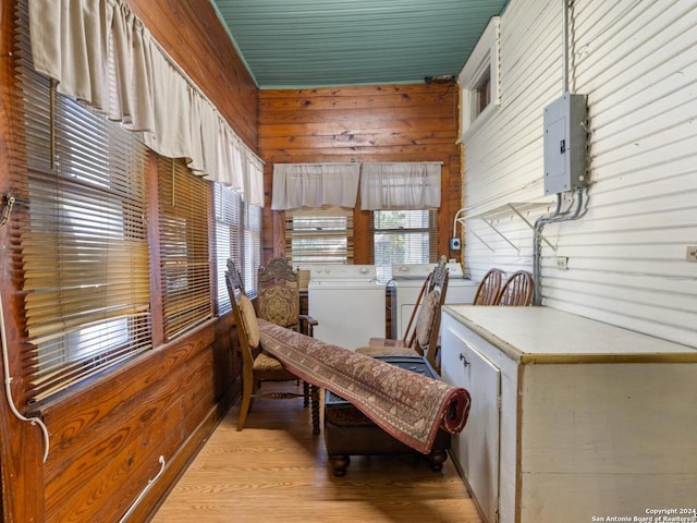 sitting room with a healthy amount of sunlight, washer and clothes dryer, light hardwood / wood-style floors, wooden walls, and electric panel