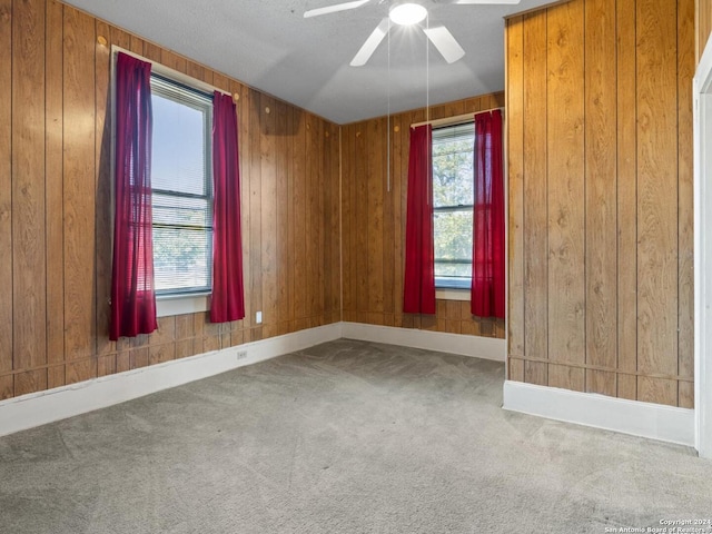 carpeted spare room featuring ceiling fan, a textured ceiling, and wooden walls