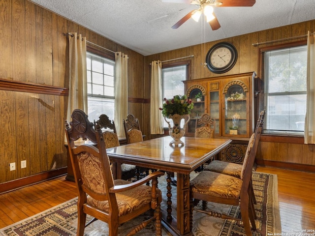 dining space featuring wood walls, hardwood / wood-style flooring, a textured ceiling, and ceiling fan