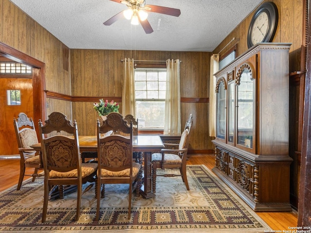 dining room featuring wooden walls, a textured ceiling, light wood-type flooring, and ceiling fan