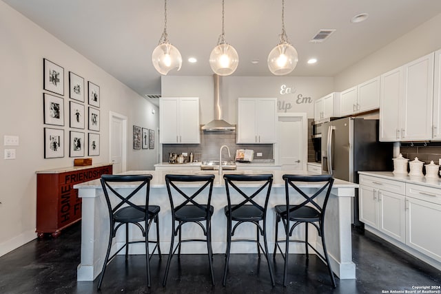 kitchen with an island with sink, wall chimney range hood, backsplash, and white cabinets