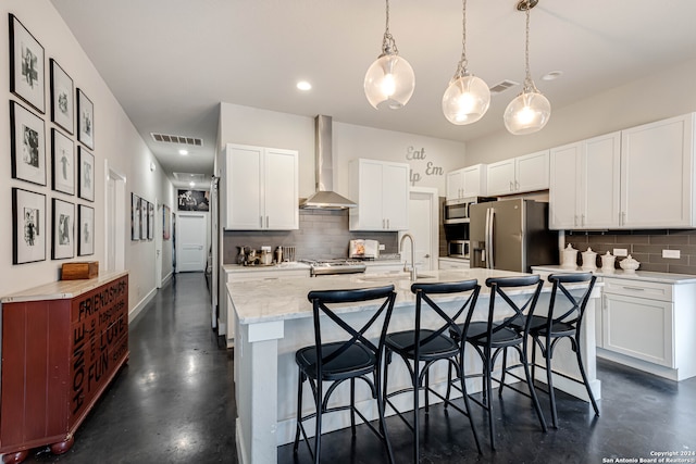 kitchen featuring hanging light fixtures, white cabinets, wall chimney range hood, and backsplash