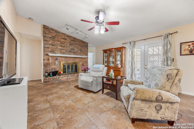 tiled living room with rail lighting, ceiling fan, a textured ceiling, vaulted ceiling, and a fireplace