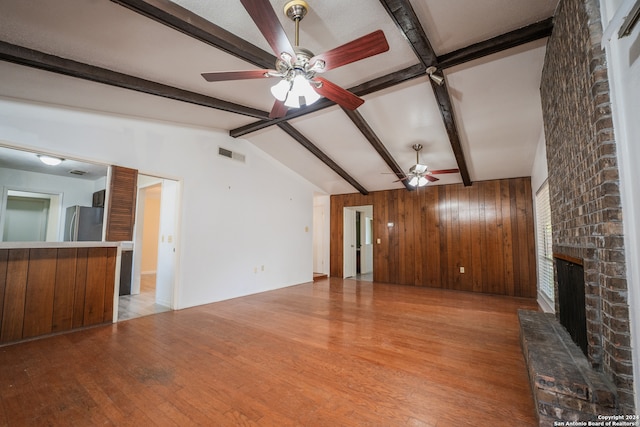 unfurnished living room featuring wood walls, a fireplace, lofted ceiling with beams, ceiling fan, and light hardwood / wood-style floors