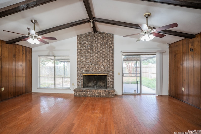 unfurnished living room featuring lofted ceiling with beams, a fireplace, hardwood / wood-style flooring, and wood walls