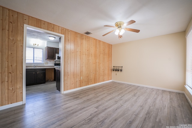 empty room featuring light wood-type flooring, wooden walls, and ceiling fan