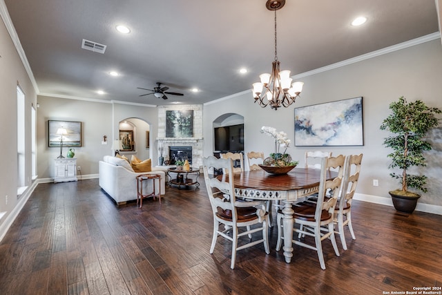 dining room with ornamental molding, dark hardwood / wood-style floors, a large fireplace, and ceiling fan with notable chandelier