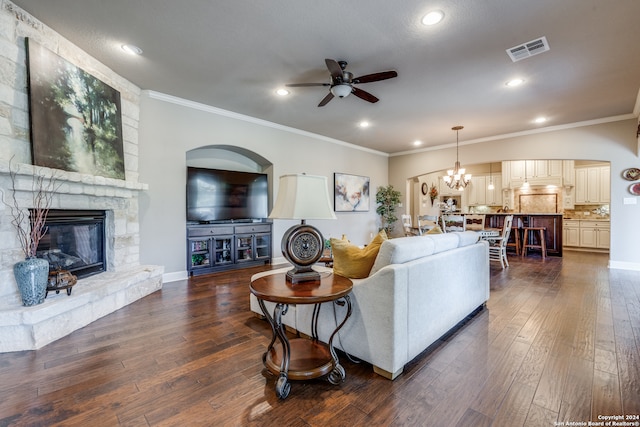 living room featuring a stone fireplace, ornamental molding, dark hardwood / wood-style flooring, and ceiling fan with notable chandelier