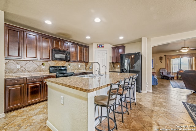 kitchen featuring tasteful backsplash, black appliances, a breakfast bar area, and a kitchen island with sink