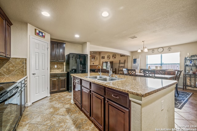 kitchen with dark brown cabinets, sink, an island with sink, and decorative backsplash