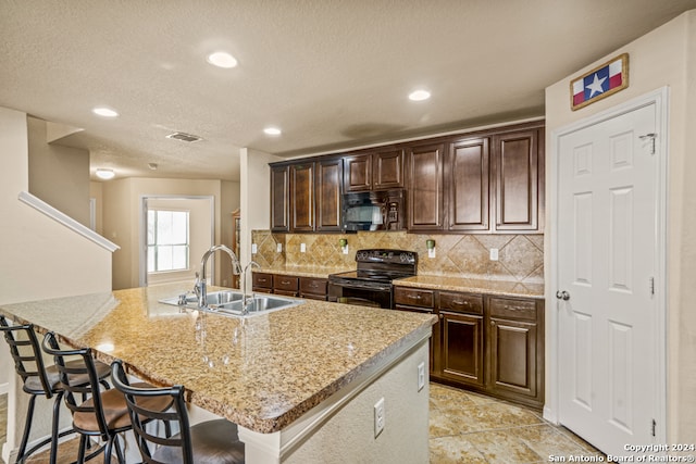 kitchen with black appliances, sink, light stone counters, a breakfast bar area, and a center island with sink