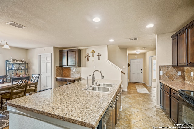 kitchen with sink, a kitchen island with sink, a textured ceiling, and tasteful backsplash