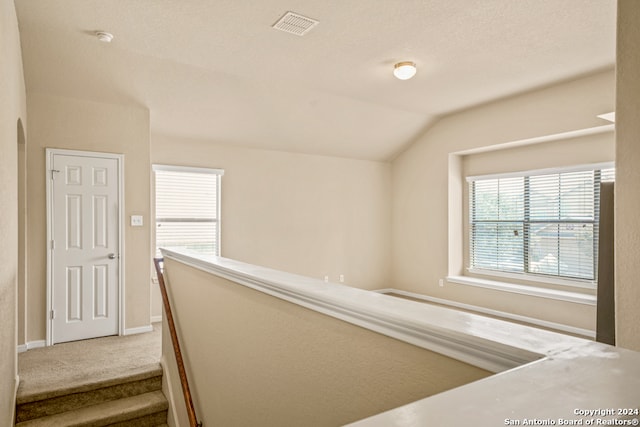 hallway with a textured ceiling, vaulted ceiling, and carpet flooring